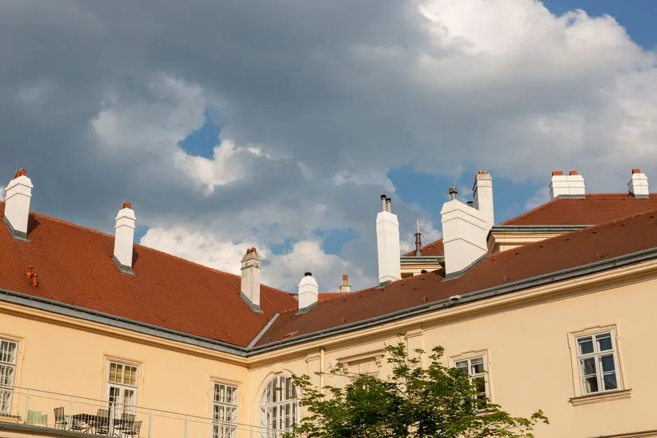 View of European architecture with red-tiled roofs and chimneys against a dramatic cloudy sky.